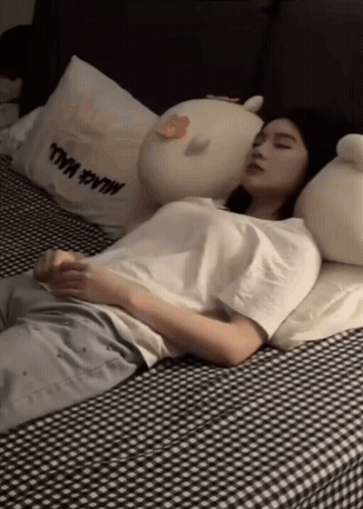 Woman Sleeping On Bed With Stuffed Animals And Black Wall Pillow GIF