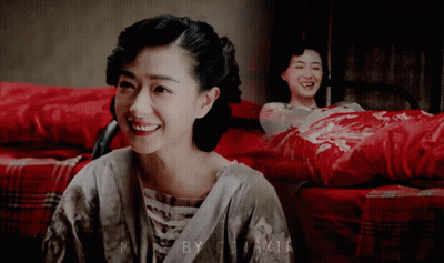 Woman Smiling In Front Of Picture Of Woman On Bed With Red Blanket GIF