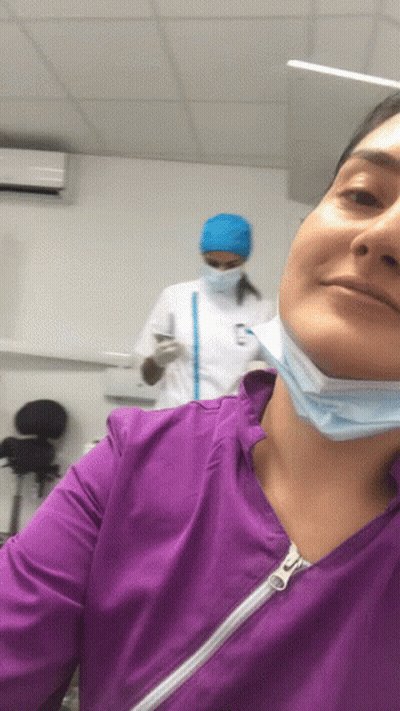 Woman Smiling In Purple Scrub Top And Face Mask GIF