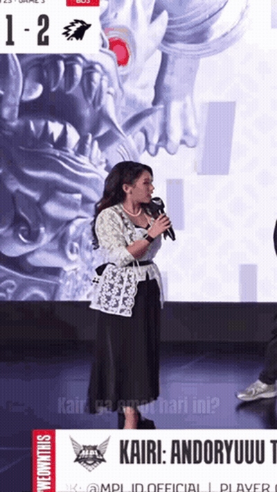 Woman Speaking Into Microphone In Front Of Kairi Andoryuu Poster GIF