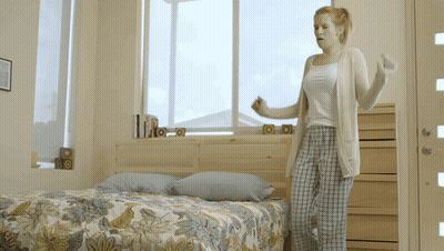 Woman Standing By Bed With Floral Comforter GIF
