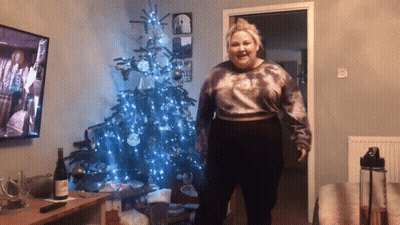 Woman Standing In Front Of Christmas Tree With Wine GIF