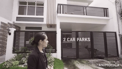 Woman Standing In Front Of House With Fence And Car Park GIF