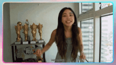 Woman Standing In Front Of Window With Trophies GIF