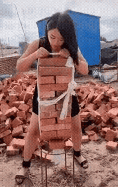 Woman Standing Next To Pile Of Bricks Holding Brick GIF