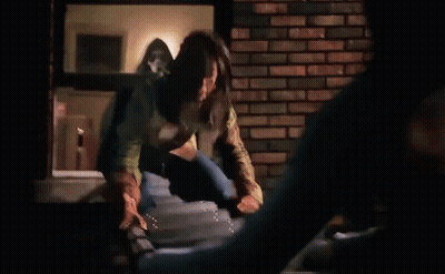 Woman Standing On Ledge Next To Brick Wall In Dark Room GIF
