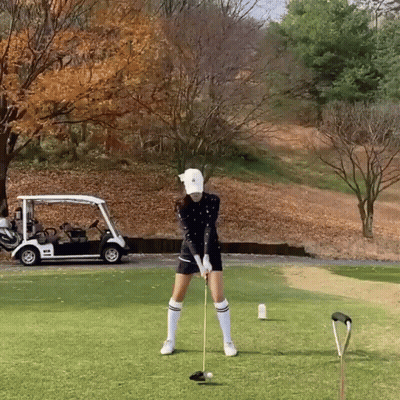 Woman Swinging Golf Club With Golf Cart In Background GIF