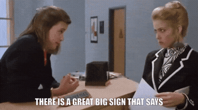 Woman Talking To Another Woman There Is A Great Big Sign That Says GIF