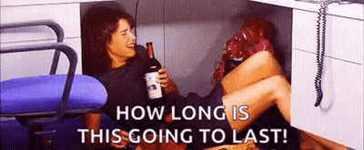 Woman Under Desk Holding Wine Saying How Long Is This Going To Last GIF