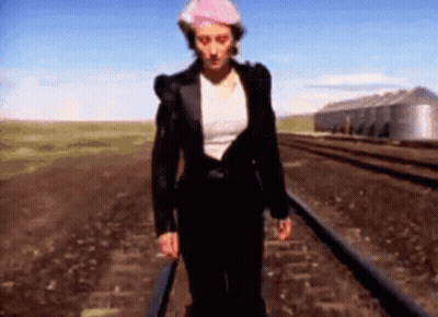 Woman Walking Train Tracks Wearing Hat GIF
