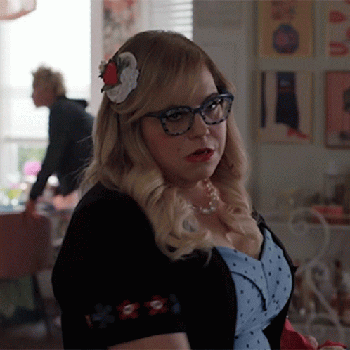 Woman Wearing Glasses And Flower In Hair Stands In Room GIF