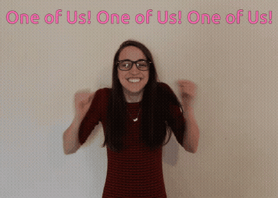 Woman Wearing Glasses In Front Of One Of Us Sign GIF