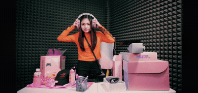 Woman Wearing Headphones In Front Of Gamer Hat And Boxes GIF