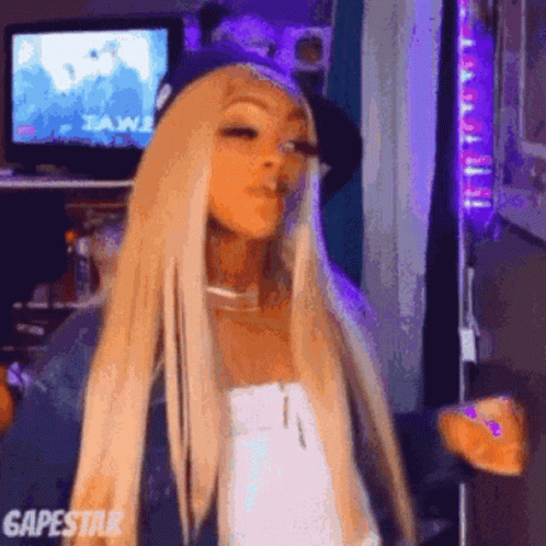 Woman With Blonde Hair And Purple Hat Standing In Front Of Television GIF