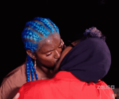 Woman With Blue Braids Kissing Woman In Red Jacket GIF