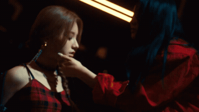 Woman With Blue Hair Touching Another Woman's Face In Dark Room GIF