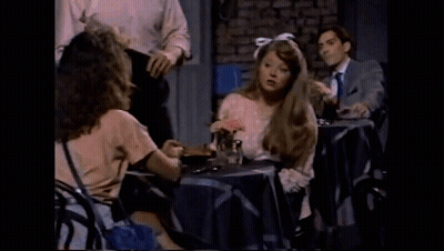 Woman With Bow In Hair Sitting At Table With Flowers And Man GIF