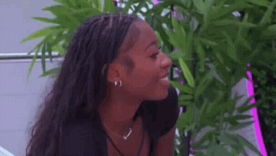 Woman With Braids And Plant Looking At Camera GIF