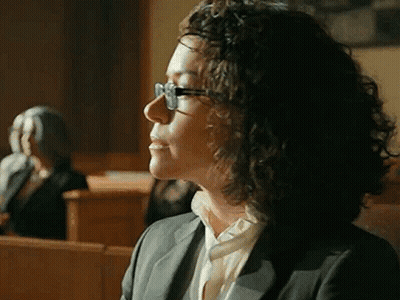Woman With Curly Hair And Glasses Sitting In Courtroom GIF