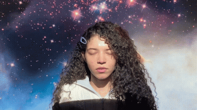 Woman With Curly Hair Eyes Closed In Front Of Galaxy GIF