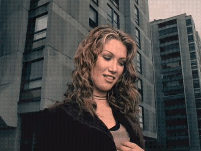 Woman With Curly Hair In Front Of Tall Building GIF