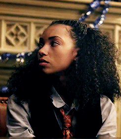 Woman With Curly Hair In Vest And Tie Sitting At Table GIF