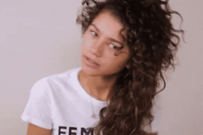 Woman With Curly Hair In White T-Shirt Looking At Camera GIF