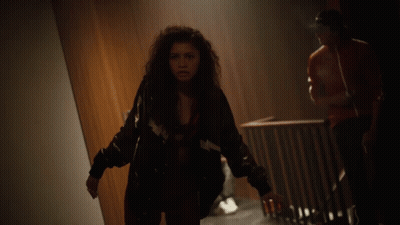 Woman With Curly Hair Looking At Camera In Dark Room GIF
