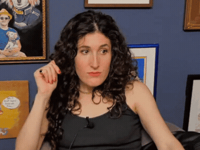 Woman With Curly Hair Sitting In Front Of Blue Wall GIF