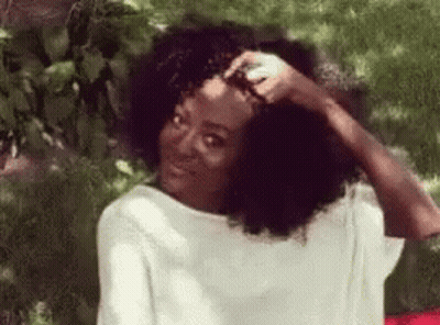 Woman With Curly Hair Sitting In Grass Hand On Head GIF