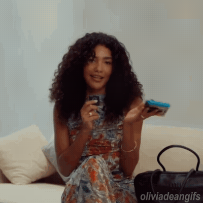 Woman With Curly Hair Sitting On Couch Holding Cell Phone GIF