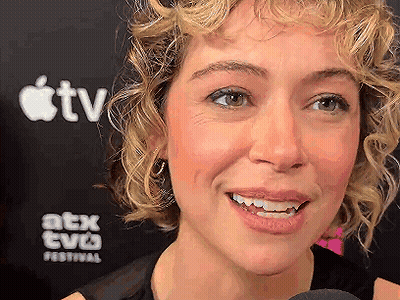Woman With Curly Hair Smiling In Front Of Apple TV Sign GIF