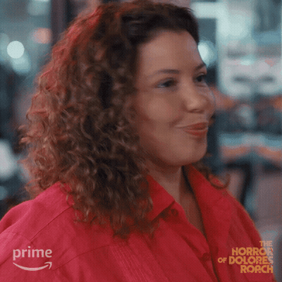 Woman With Curly Hair Smiling In Red Shirt From The Horror Of Dolores Roach GIF