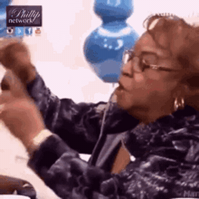 Woman With Glasses And Blue Jacket Sitting On Couch Holding Remote GIF