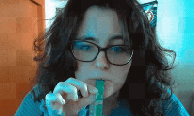 Woman With Glasses And Blue Sweater Eating Green Stick GIF