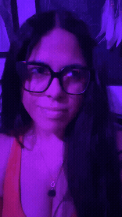 Woman With Glasses And Necklace Taking Selfie In Purple Room GIF