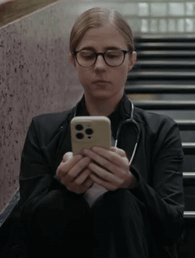 Woman With Glasses And Stethoscope Sitting On Stairs Looking At Cell Phone GIF