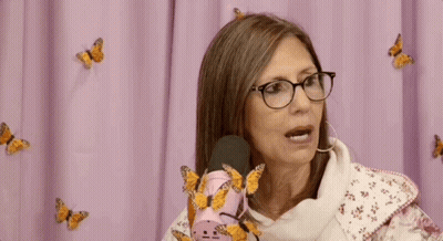 Woman With Glasses Sitting At Pink Microphone With Butterflies GIF