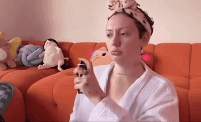 Woman With Headband Spraying Face On Orange Couch GIF