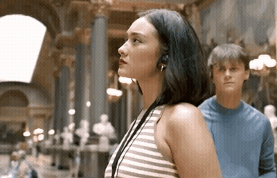 Woman With Headphones Next To Man In Blue Shirt In Museum GIF