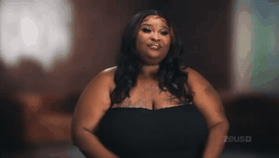 Woman With Large Breasts In Black Dress Looking At Camera GIF