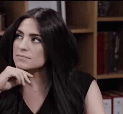 Woman With Long Black Hair Sitting In Front Of Bookshelf GIF