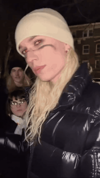 Woman With Long Blonde Hair In White Beanie And Black Jacket GIF