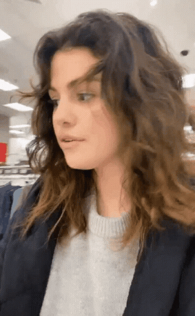 Woman With Long Curly Hair In Sweater And Jacket In Store GIF