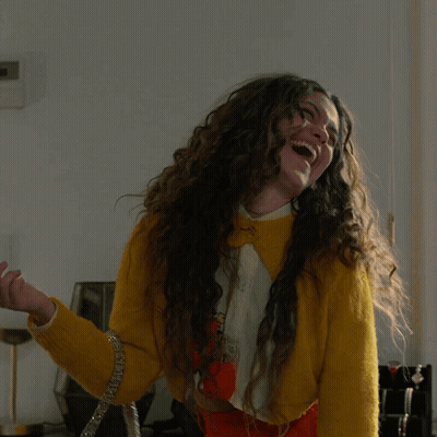 Woman With Long Curly Hair In Yellow Sweater And Orange Skirt GIF