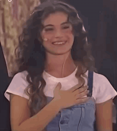 Woman With Long Curly Hair Smiling Hand On Chest GIF