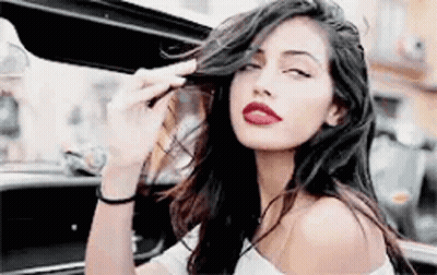 Woman With Long Hair And Red Lips Sitting In Car With Open Door GIF