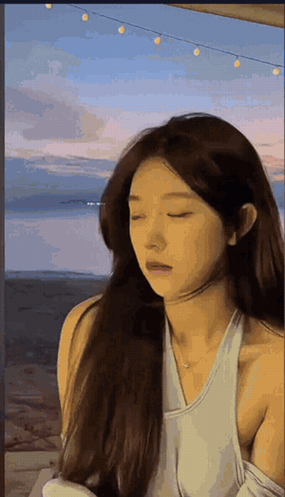 Woman With Long Hair Standing In Front Of Water Eyes Closed White Tank Top GIF
