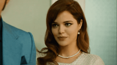 Woman With Pearl Necklace And Earrings Looks At Man In Blue Suit GIF