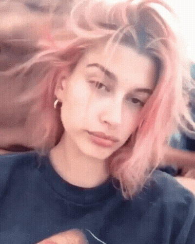 Woman With Pink Hair In Blue Shirt And Earrings Looking At Camera GIF